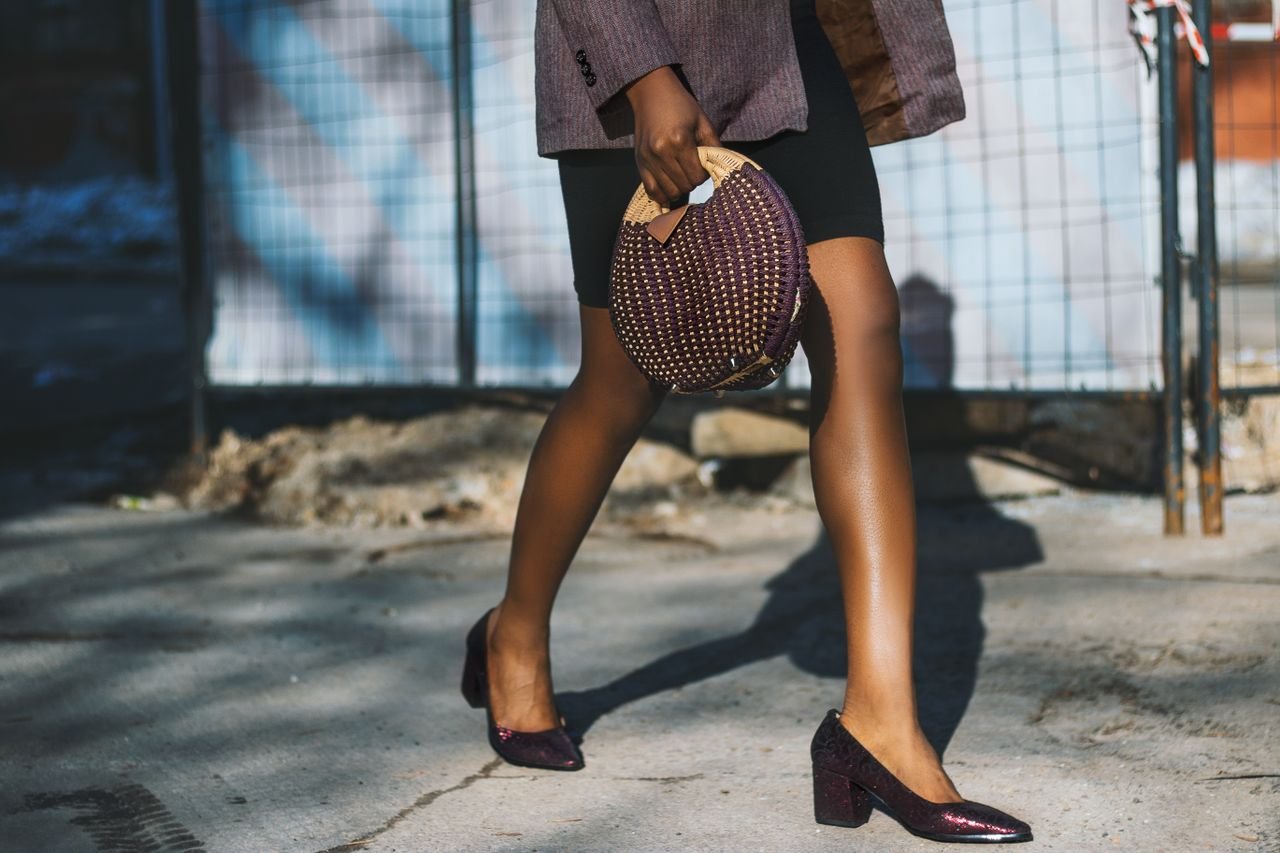 Fashionable woman in heels and chic bag walking on sunny street.